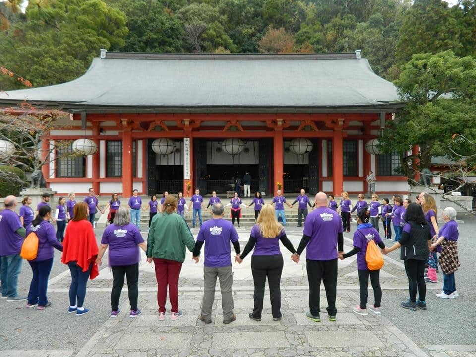 Grupo de pessoas de mãos dada, formando um círculo, em frente a um templo japonês.