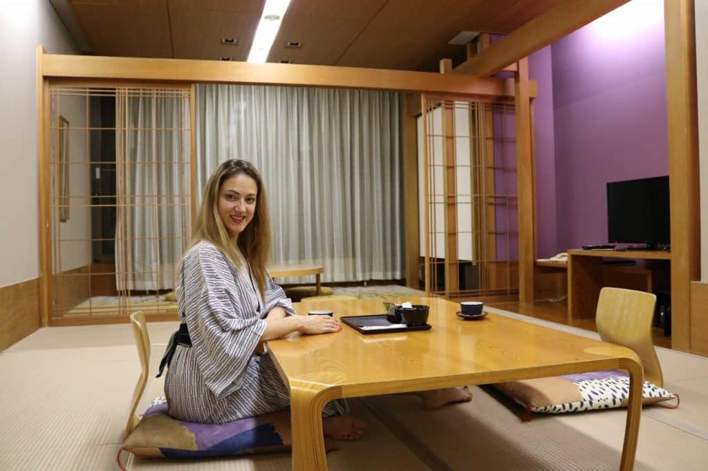 Mulher sentada em almofada no chão, em frente a uma mesa de madeira baixa, com xícaras de chá.