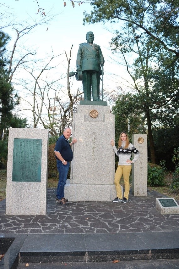 Um homem e uma mulher ao lado de uma estátua de um homem, com pedestal alto.