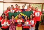 Grupo de pessoas com camisetas vermelhas, segurando uma bandeira do Brasil.