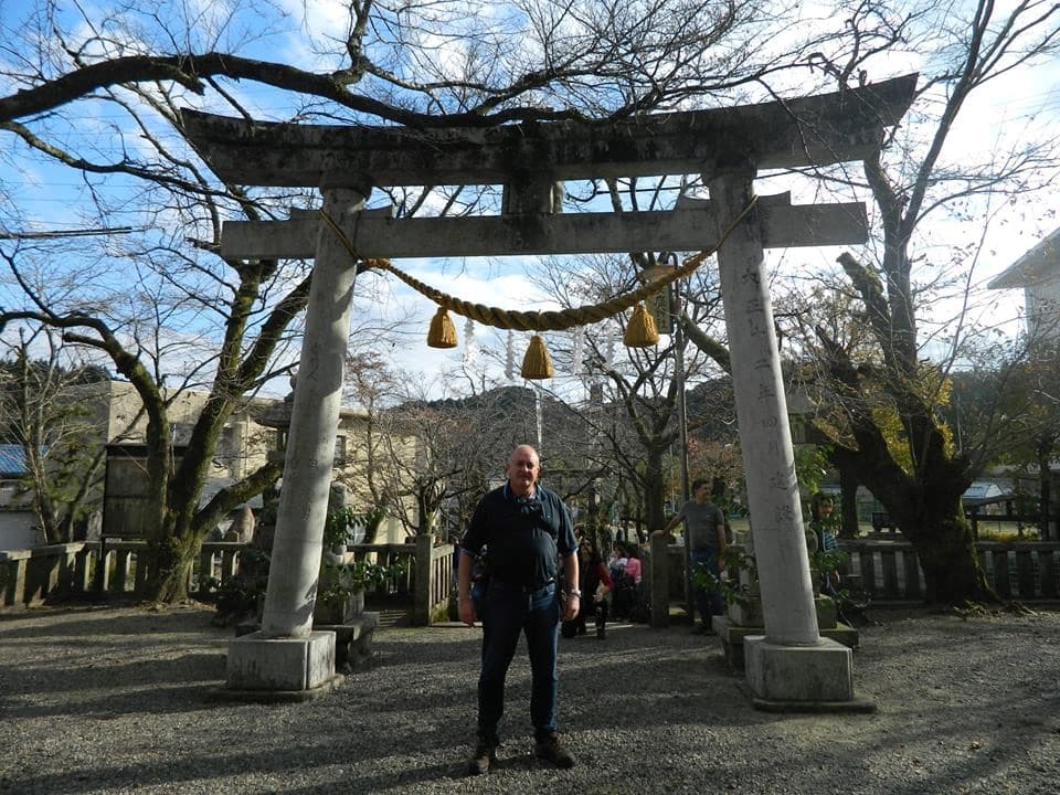 Homem de pé em frente a portal de templo japonês.