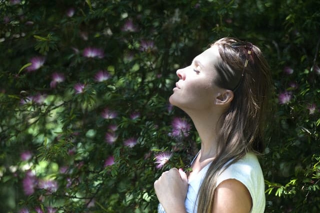 Mulher de perfil com rosto para cima com sol refletindo de olhos fechados