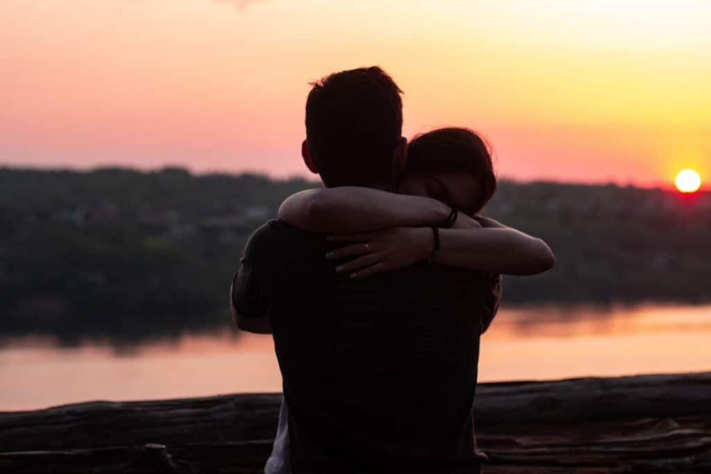 Homem e mulher se abraçando sob o pôr do sol.