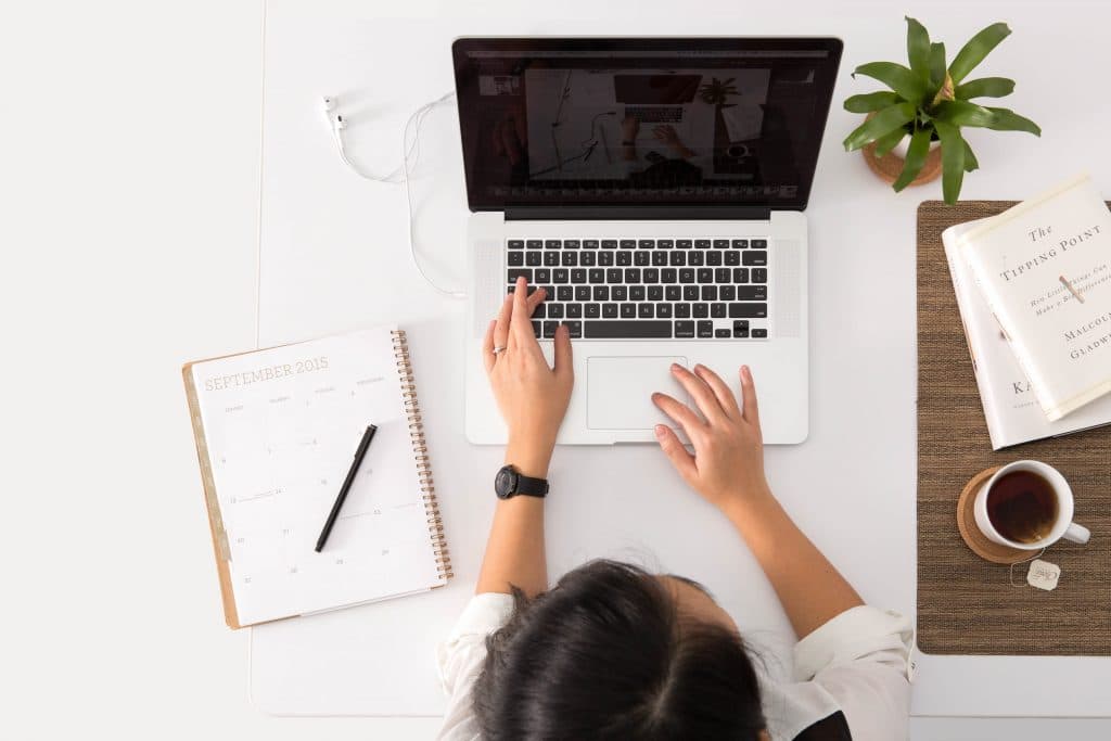 Pessoa sentada em uma mesa com um computador e cadernos, estudando