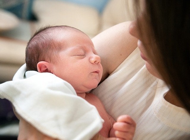 Bebê recém nascido dormindo em colo de mulher.