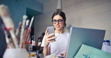 Mulher em seu escritório olhando para o seu celular feliz