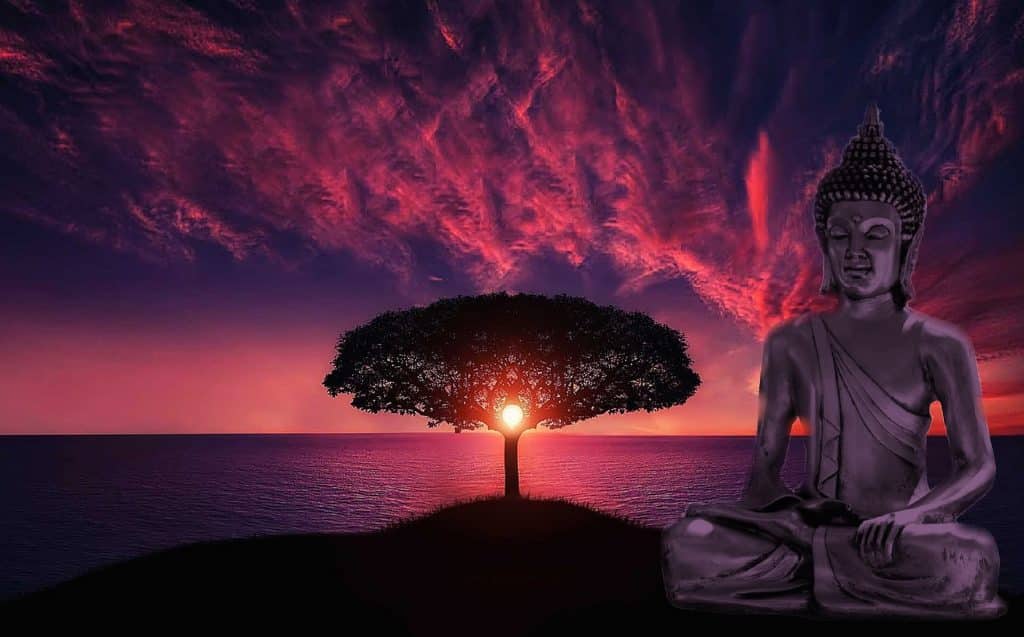 Imagem de Buda em posição de meditação. Ao fundo temos um lago, uma árvore com copa bem frondosa e um lindo por do sol.