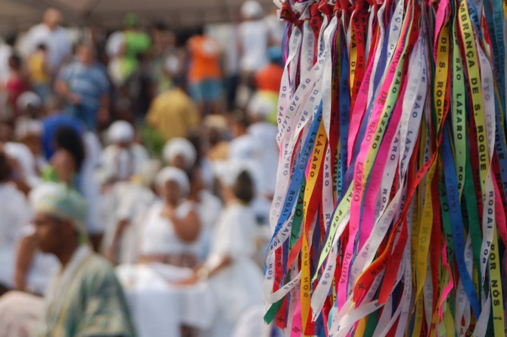 Imagem de um ritual de Candomblé. Várias fitas coloridas e ao fundo mães e pais de santos.
