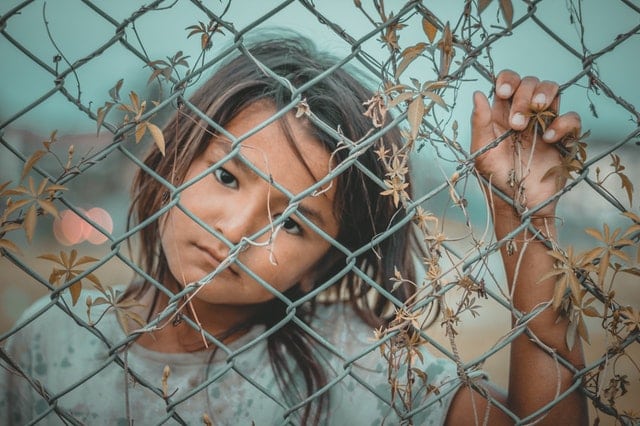 Garota vistas por tás de grade com mão apoiada e expressão triste