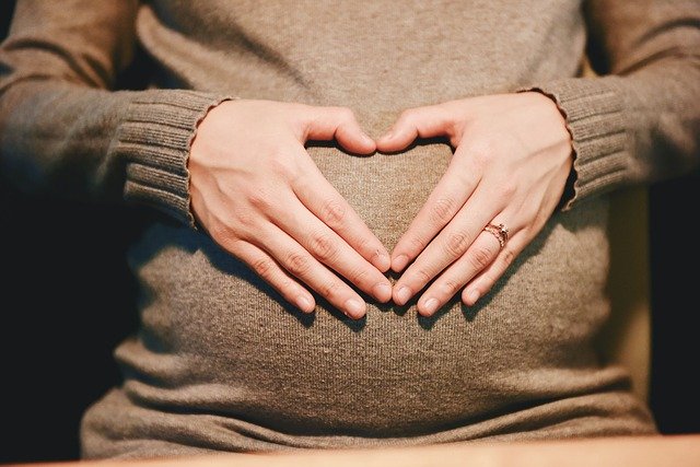 Mulher grávida com mãos na barriga em formato de coração