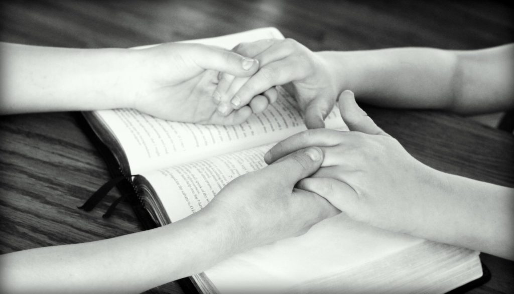 Imagem em preto e branco de mãos dadas sobre uma bíblia aberta. Luto imagem.
