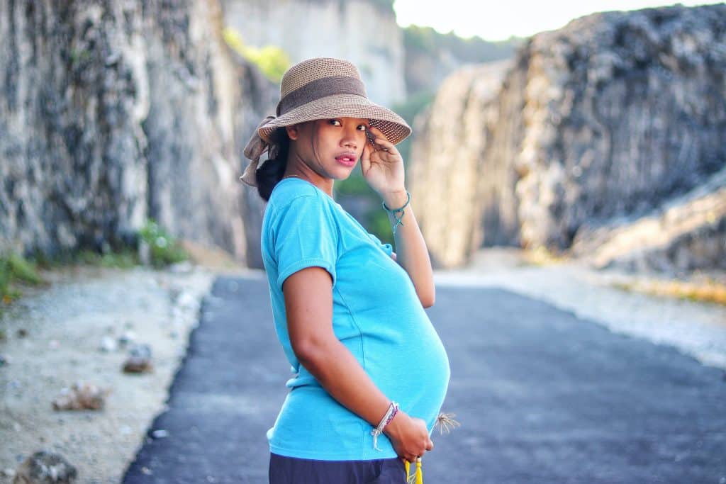Mulher grávida de perfil. Ela está vestindo uma camiseta azul e um chapéu bege.