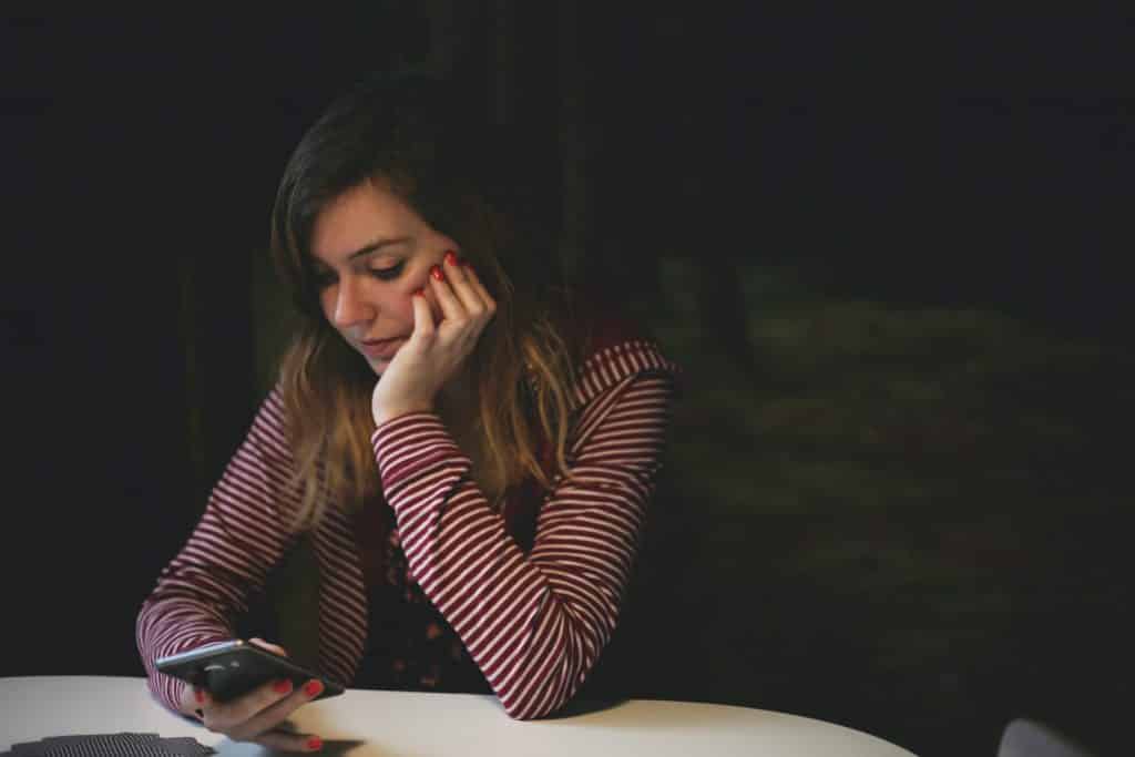 Mulher pensativa apoiando seu rosto com sua mão e olhando para o celular 