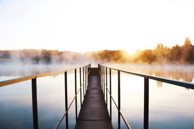 Ponte com rio embaixo e neblina com sol refletindo 