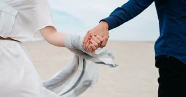 Homem e mulher correndo na praia de mãos dadas