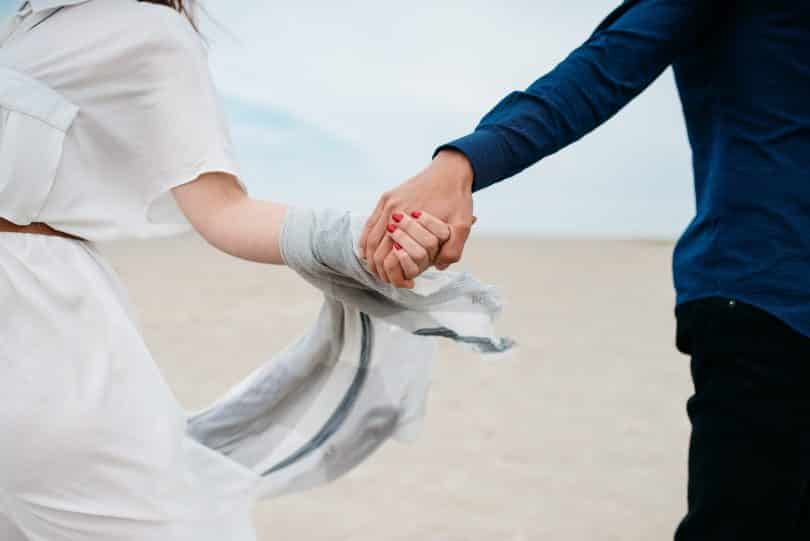 Homem e mulher correndo na praia de mãos dadas