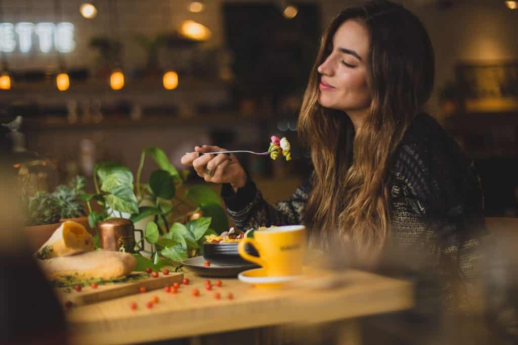 Mulher jantando sozinha em uma mesa com vários alimentos