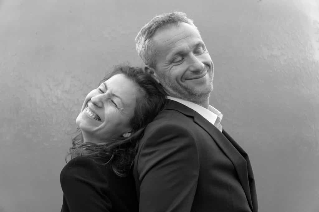 Imagem em preto e branco de um casal homem e mulher de meia idade. Eles estão de costas um para outro e estão felizes.