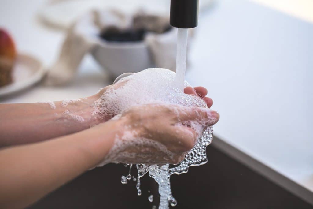 Pessoa lavando as mãos em uma torneira.