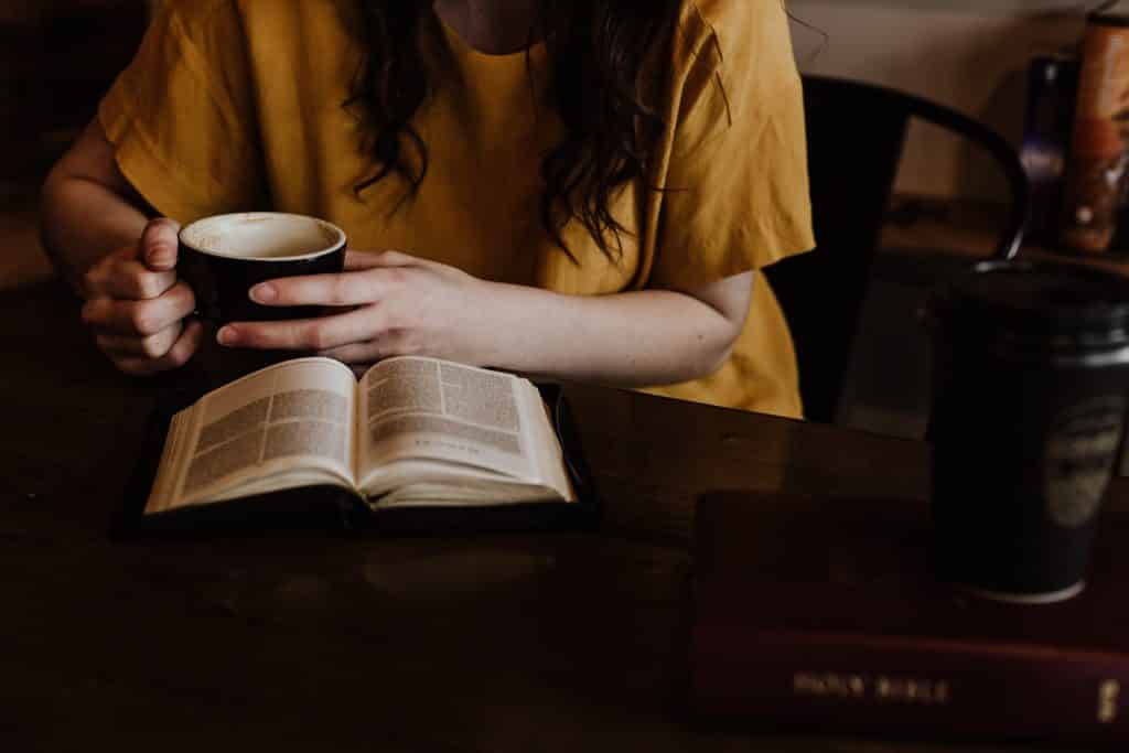 Mulher tomando xícara de café com um livro aberto em seu colo