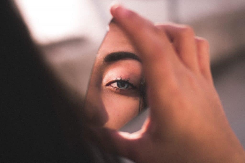 Foto de uma mulher segurando um espelho quebrado, que reflete a figura de seu olho.