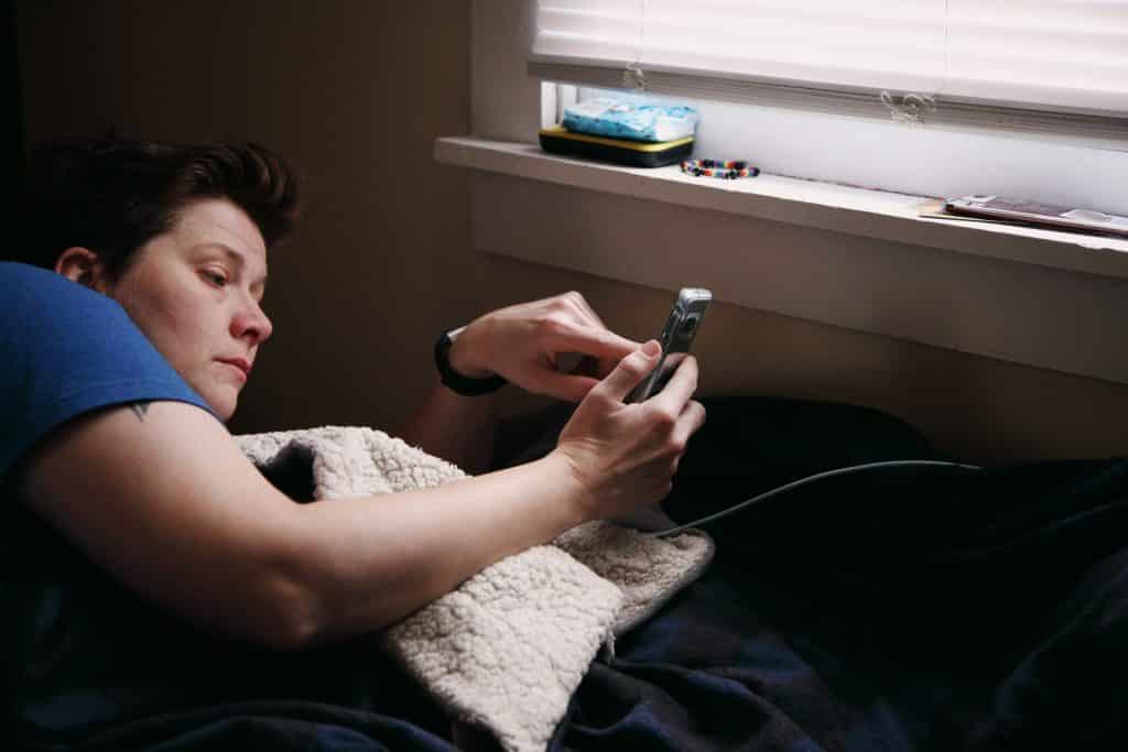 Mulher deitada na cama usando o telefone celular, durante a quarentena.