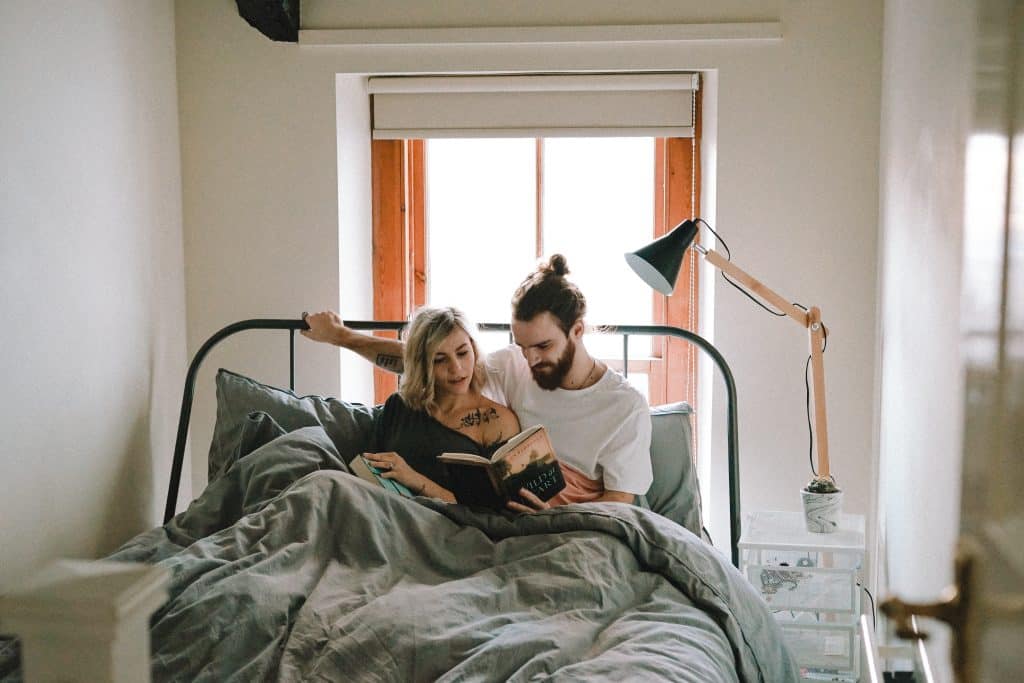 Homem e mulher sentados na cama lendo um livro.