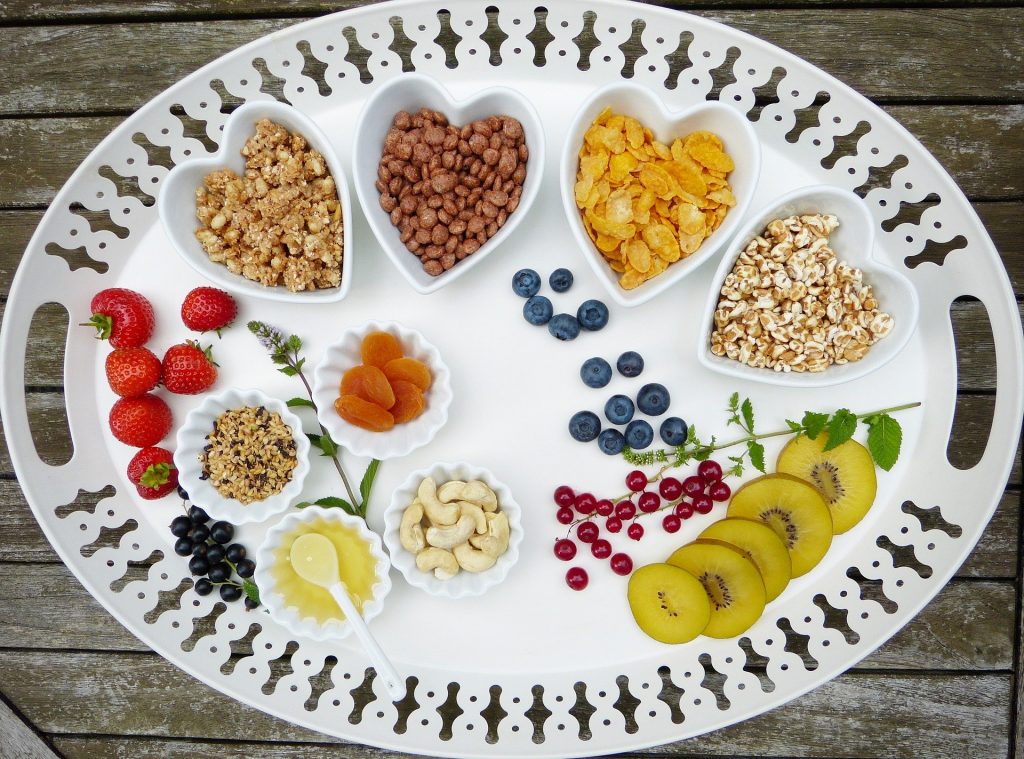 Imagem de um prato grande branco dividido em várias porções com alimentos variados como: frutas, grãos, sementes, óleos.