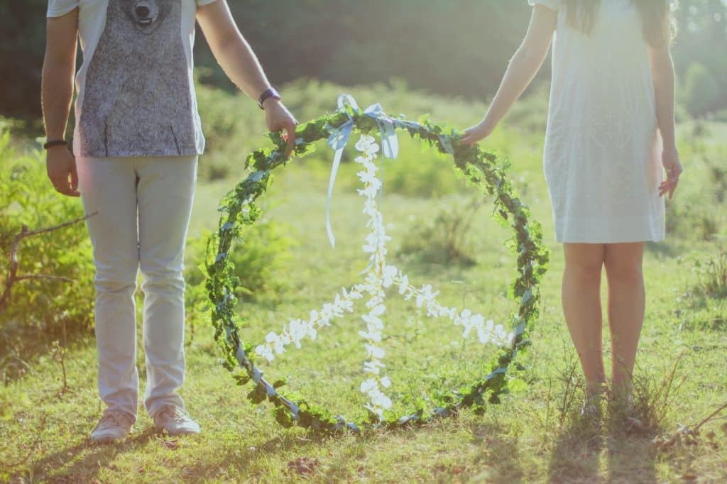 Duas pessoas segurando arco com o símbolo da paz, feito com folhas verdes e flores brancas.