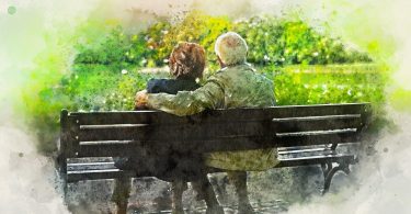 Imagem de um casal de idosos (avós) sentacdos em um banco de mandeira olhando para um lindo jardim.