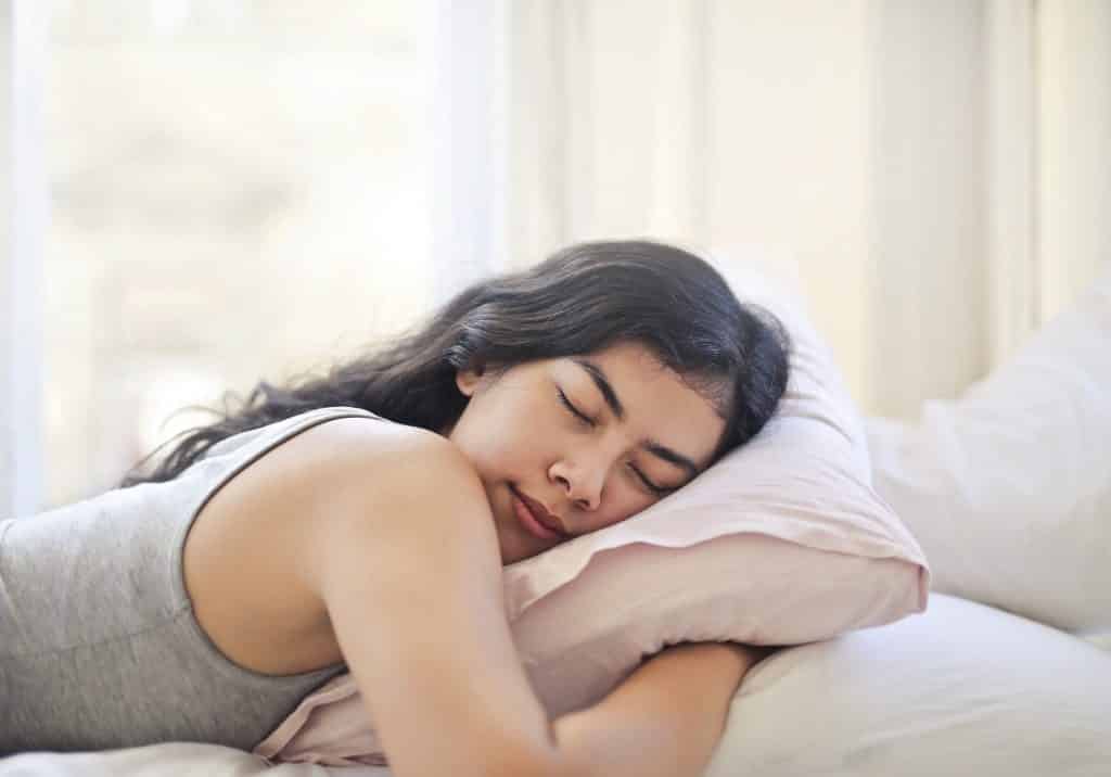 Mulher deitada na cama, de bruços, dormindo enquanto abraça o travesseiro.