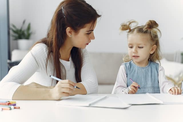 Mãe e filha desenhando em cadernos em mesa