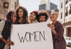 Mulheres na rua segurando cartaz escrito em inglês "women"
