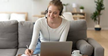 Mulher olhando para o computador sorrindo sentada no sofá