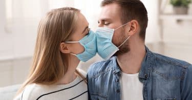 Casal em quarentena, beijando-se com máscaras faciais de proteção.