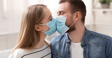 Casal em quarentena, beijando-se com máscaras faciais de proteção.