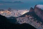 Vista aérea do Rio de Janeiro, do lado direito, uma favela acesa em topo de morro, enquanto na parte de baixo, perto do mar, prédios grandes de classe alta.