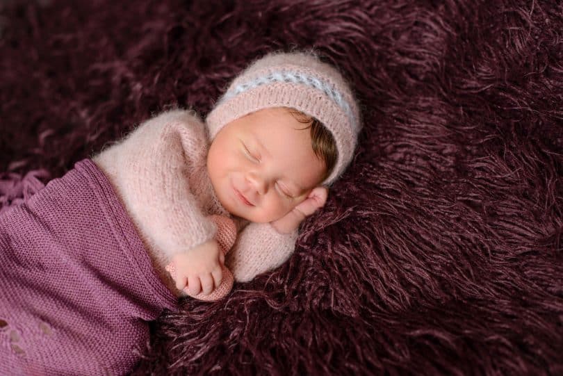 Bebê recém-nascido, enrolado em cobertores, esboçando um sorriso.