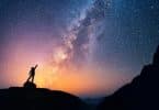 Silhueta de pessoa em montanha com céu estrelado ao fundo