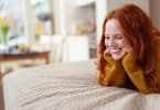 Mulher sorrindo deitada na cama com as mãos apoiando a cabeça