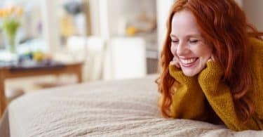 Mulher sorrindo deitada na cama com as mãos apoiando a cabeça