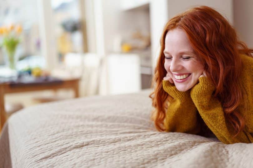 Mulher sorrindo deitada na cama com as mãos apoiando a cabeça