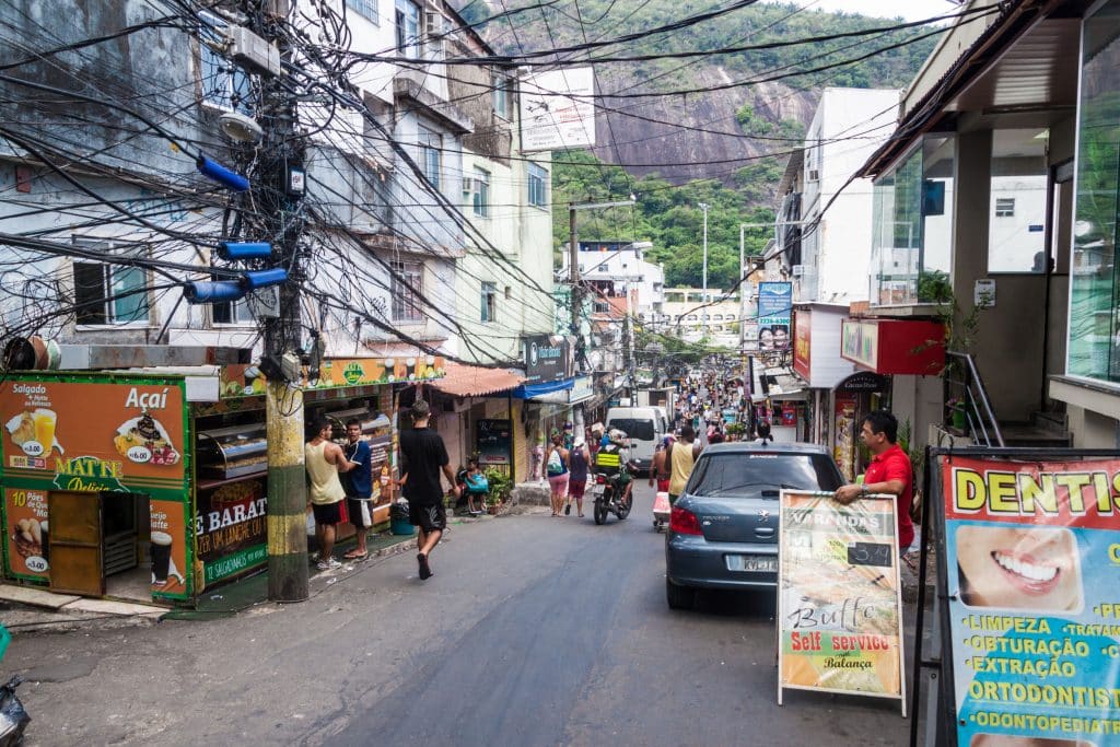 Rua em meio de favela, com muitas pessoas andando a pé.