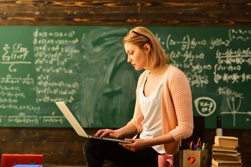 Professora sentada em sua mesa da sala de aula usando notebook