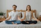 Imagem de um casal meditando no quarto, sobre a cama.