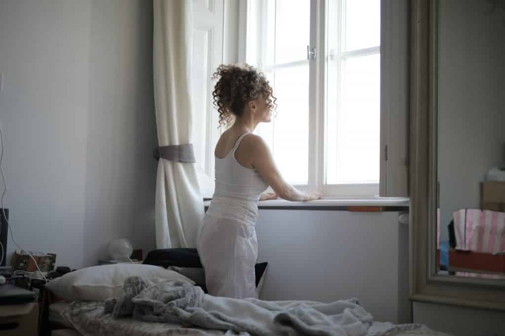 Mulher de cabelos cacheados em um quarto, olhando pela janela.