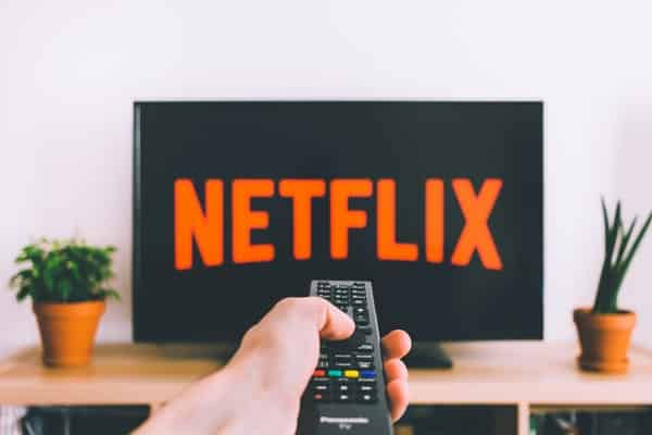 Mão segurando controle apontando para TV ligada no início da Netflix