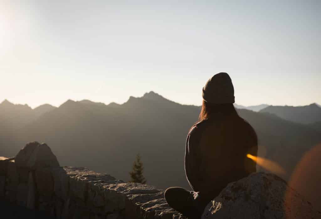 Mulher sentada em uma montanha olhando para o sol