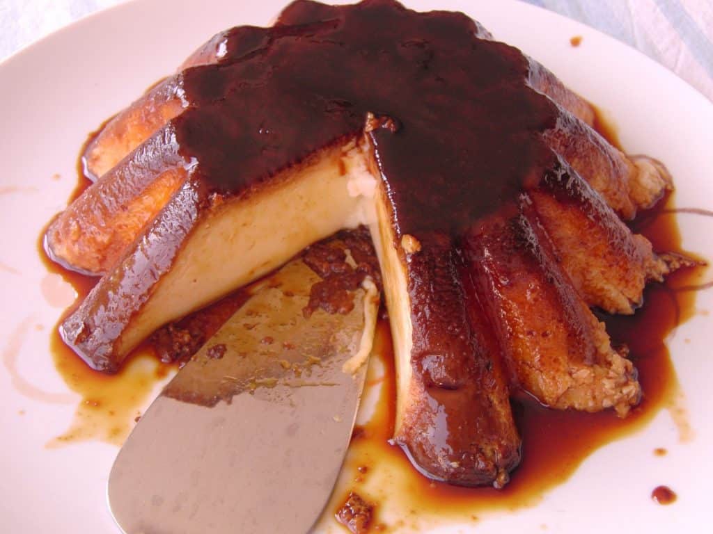 Imagem de um pudim feito de pinhão. Ele está sobre um prato brancp e já está cortado pronto para ser consumido.