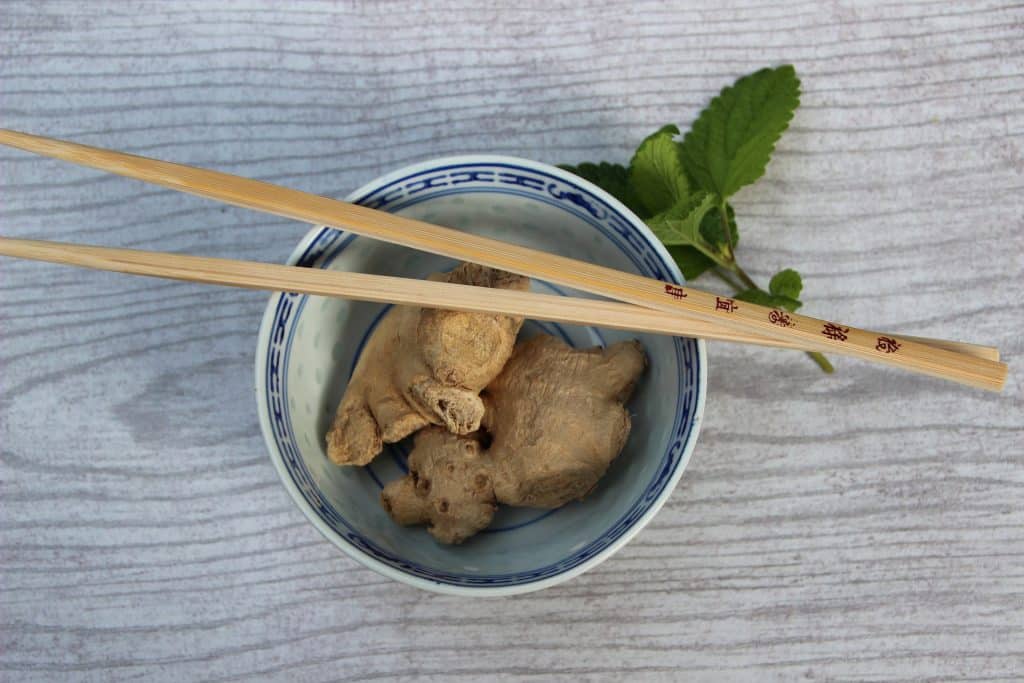 Imagem de um bowl de porcelana brnaca comdois pedaços de gengibre. Ao lado folha de hortelã. O gengibre será usado como ingrediente para a produção de remédio caseiro para o vitiligo.
